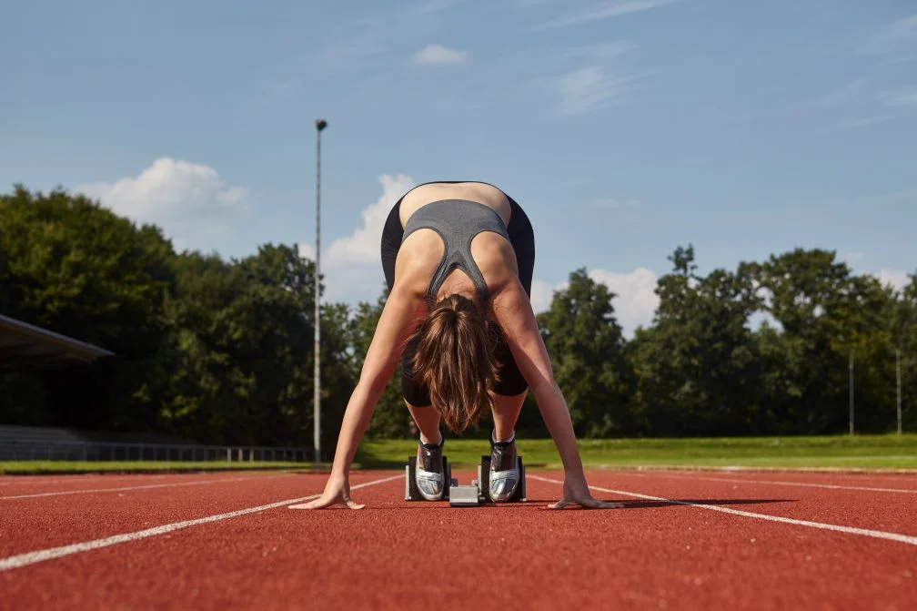  Young female runner bending forward on race track starting line 